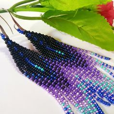 two purple and blue seed beaded earrings next to a green leaf on a white surface