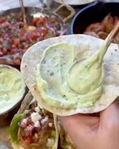 a hand holding a tortilla with guacamole and salsa in the background