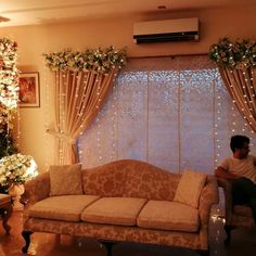 a man sitting on top of a couch in front of a window covered in christmas lights