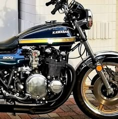 a black and blue kawasaki motorcycle parked in front of a white brick building with gold rims