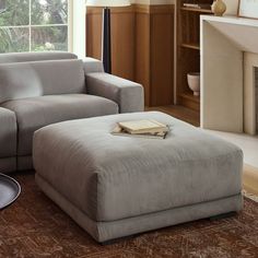 a living room with a couch, ottoman and book on the floor in front of a fireplace