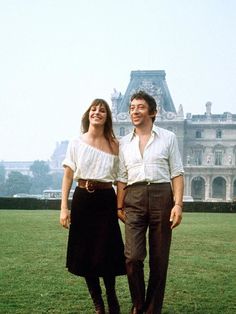 a man and woman standing in front of a large building on top of a lush green field