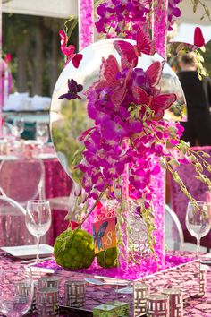 the table is decorated with pink flowers and purple butterflies in glass vases, along with wine glasses