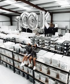 two people are sitting on a shelf in a warehouse