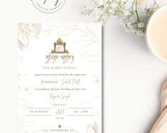 a white and gold wedding card on top of a table next to a cup of coffee