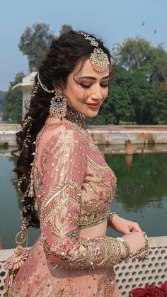 a woman in a pink lehenga standing by the water