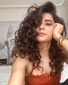 a woman sitting on top of a bed wearing a red dress and gold bracelets