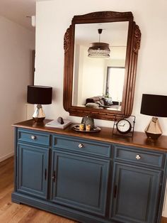 a blue dresser with a mirror on top of it and lamps in front of it