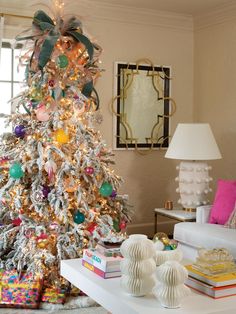 a decorated christmas tree in the corner of a living room with white furniture and colorful decorations