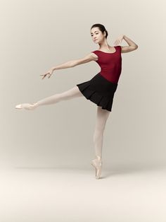 a woman in a red shirt and black skirt is doing a ballet pose with her legs spread out