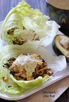 two lettuce wraps filled with meat and vegetables on a plate next to an avocado