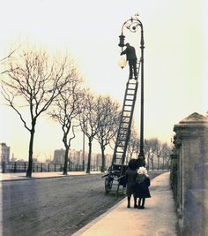 two people are standing on a ladder near a street light and lamp post in an old photo