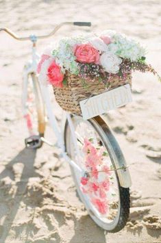 a bicycle with flowers in the basket is parked on the beach