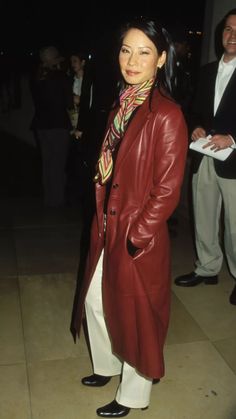 a woman in a red leather coat and white pants standing on a tile floor at night