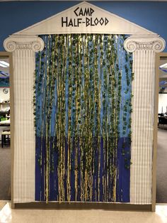 the entrance to an office building decorated with greenery and gold foil streamers that spell out camp half - blood