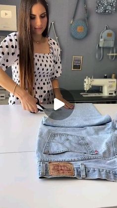 a woman is standing in front of a table with some jeans on it and a sewing machine next to her