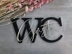 the word w is spelled in cursive writing on a gray surface next to dried flowers