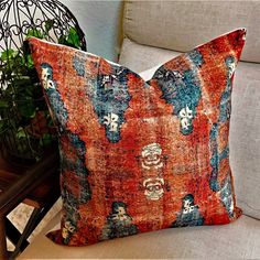 an orange and blue pillow sitting on top of a white couch next to a potted plant