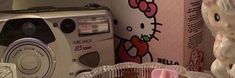 a hello kitty camera sitting next to a box and some cupcakes on a table