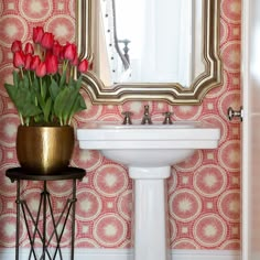 a white pedestal sink sitting under a mirror next to a vase with flowers in it