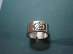 the avengers symbol is engraved on this silver and gold ring, which sits atop a green surface