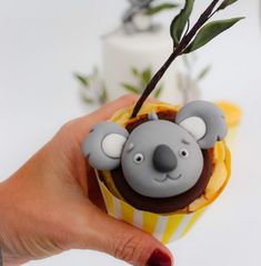 a hand holding a cupcake with a koala decoration on it