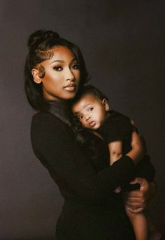 a woman holding a baby in her arms and posing for the camera with dark background