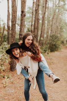 two girls are playing in the woods with one girl on her back and another girl carrying her