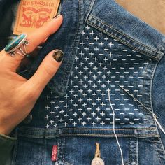 a woman's hand holding onto an american flag patched jean jacket with buttons