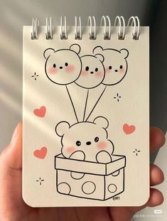 a hand holding a notebook with a drawing of two teddy bears in a box on it