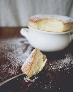 a powdered sugar covered pastry sitting in a white bowl next to a spoon on a wooden table