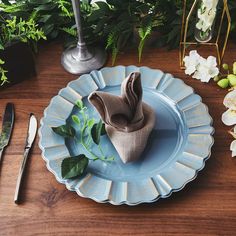 a blue plate topped with a napkin next to silver utensils and greenery