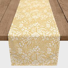 a wooden table topped with a yellow and white flowered table runner on top of it