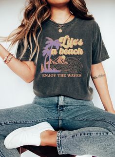 "Introducing our \"Life Is A Beach\" t-shirt, the perfect addition to your summer wardrobe. This stylish and comfortable beach life shirt is a must-have for any beach-goer or vacation enthusiast. Featuring a retro surf design, this cruise shirt is a timeless classic that will never go out of style. The vibrant graphic on this women's oversized tee is sure to turn heads and make a statement. Made from high-quality materials, our graphic tee is both soft and durable, ensuring long-lasting comfort and style. Whether you're lounging on the sand, cruising the waves, or just soaking up the sun, this vacation shirt is the perfect choice. T-Shirt DETAILS -Designs are professionally printed. -Comfortable relaxed fit  -100% Cotton, except heather colors (Cotton Poly blend) -Shirts are a unisex fit, Summer Surfing T-shirt, Surfing T-shirt With Front Print For Beach Season, Retro T-shirt For Surfing In Beach Season, Life Is A Beach, Womens Oversized Tee, Graphic Tee T-shirt With Front Print For Surfing, Vacation Surfing Cotton T-shirt, Retro Surf, Cruise Shirts