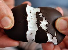 a person holding a piece of chocolate with white frosting on it's side