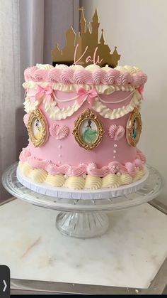 a pink and white cake with gold decorations on it's top is sitting on a table