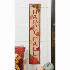 a cross stitch happy fall sign hanging on the side of a door with pumpkins and gourds