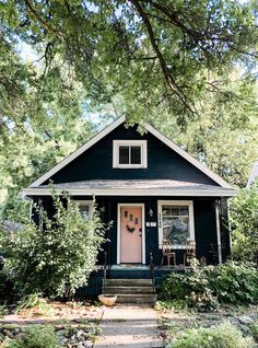 a black house with pink front door and steps leading up to the front door is surrounded by greenery