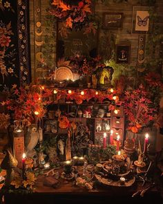 a table topped with lots of candles next to a wall covered in pictures and plants