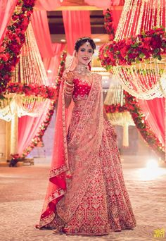 a woman in a red and gold bridal gown standing under an archway decorated with flowers