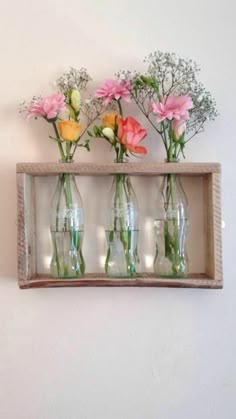 four vases with flowers in them sitting on a shelf above a wall mounted mirror