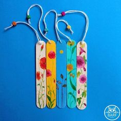 three wooden tags with flowers painted on them are hanging from strings against a blue background