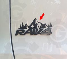 the rear end of a white car with mountains and trees on it's side