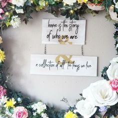 two wooden signs hanging on a wall with flowers around them and the words home is the story of who we are