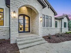 the front entrance of a home with stone steps and windows at dusk, in an upscale neighborhood