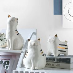 three ceramic cats sitting on top of a shelf next to a clock and other items