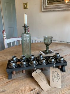 a table topped with lots of cups and a bottle filled with water next to a candle