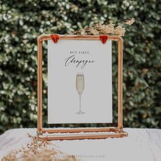 a sign that says, but first, champagne is on top of a table in front of some bushes