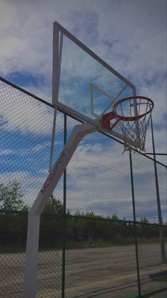 a basketball hoop is attached to the side of a fenced in area with trees and blue sky