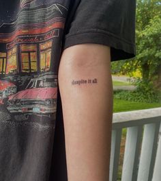 a man with a tattoo on his arm that says despite it all, there is a car parked in front of the building